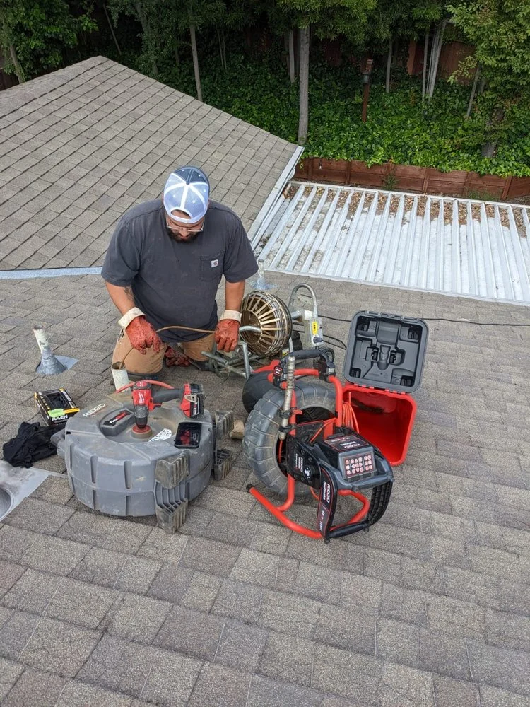 Technician with drain auger, water jetting equipment, and tools on residential roof