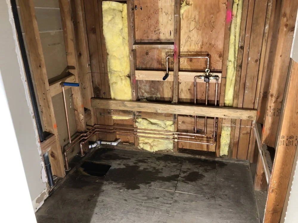 Copper plumbing lines and drain pipes installed in bathroom framing with insulation