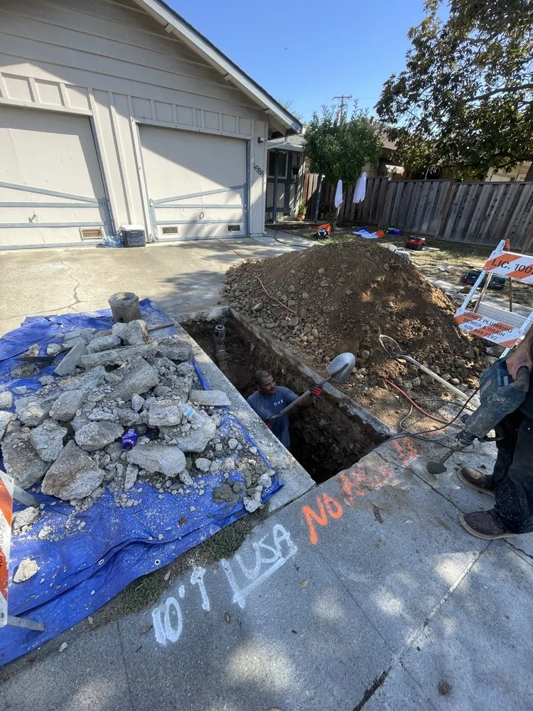 Deep sewer line excavation trench with soil and rock removal next to residential garage