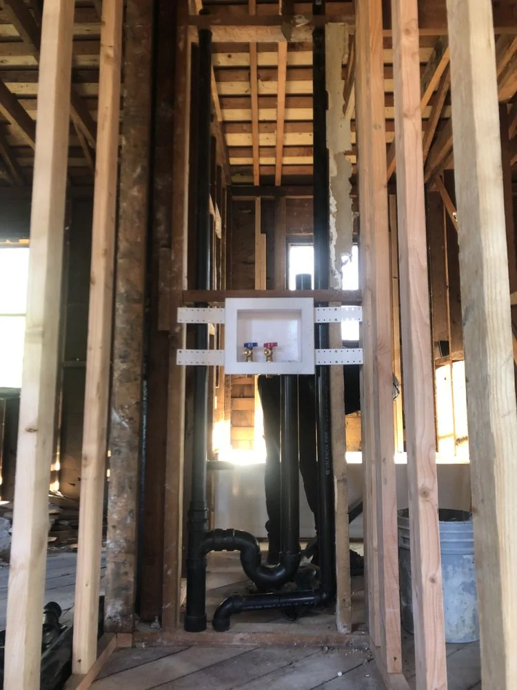 Black ABS drain pipes and white PVC vent stack installed in wood-framed wall cavity during rough-in plumbing phase