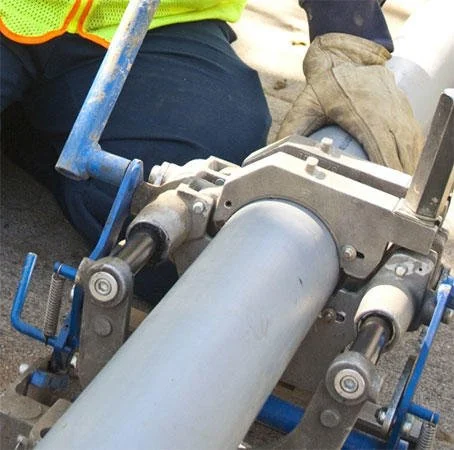 Technician operating motorized drain auger on PVC pipe with blue equipment clamps