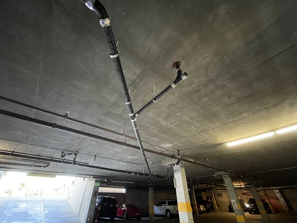 Black PVC drain pipes with metal straps installed on concrete parking structure ceiling